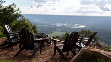Un espacio al aire libre con vistas a un valle, equipado con sillones Adirondack y una chimenea.