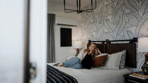 A bedroom with a bed, a headboard, a nightstand, a lamp, and a wall with a leaf pattern. - Unique Container with BBQ Ideal for Couples in Georgia (Rising Fawn)