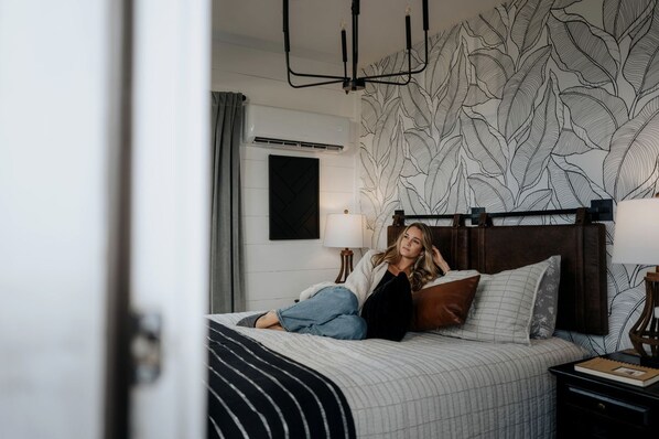 A bedroom with a bed, a headboard, a nightstand, a lamp, and a wall with a leaf pattern.