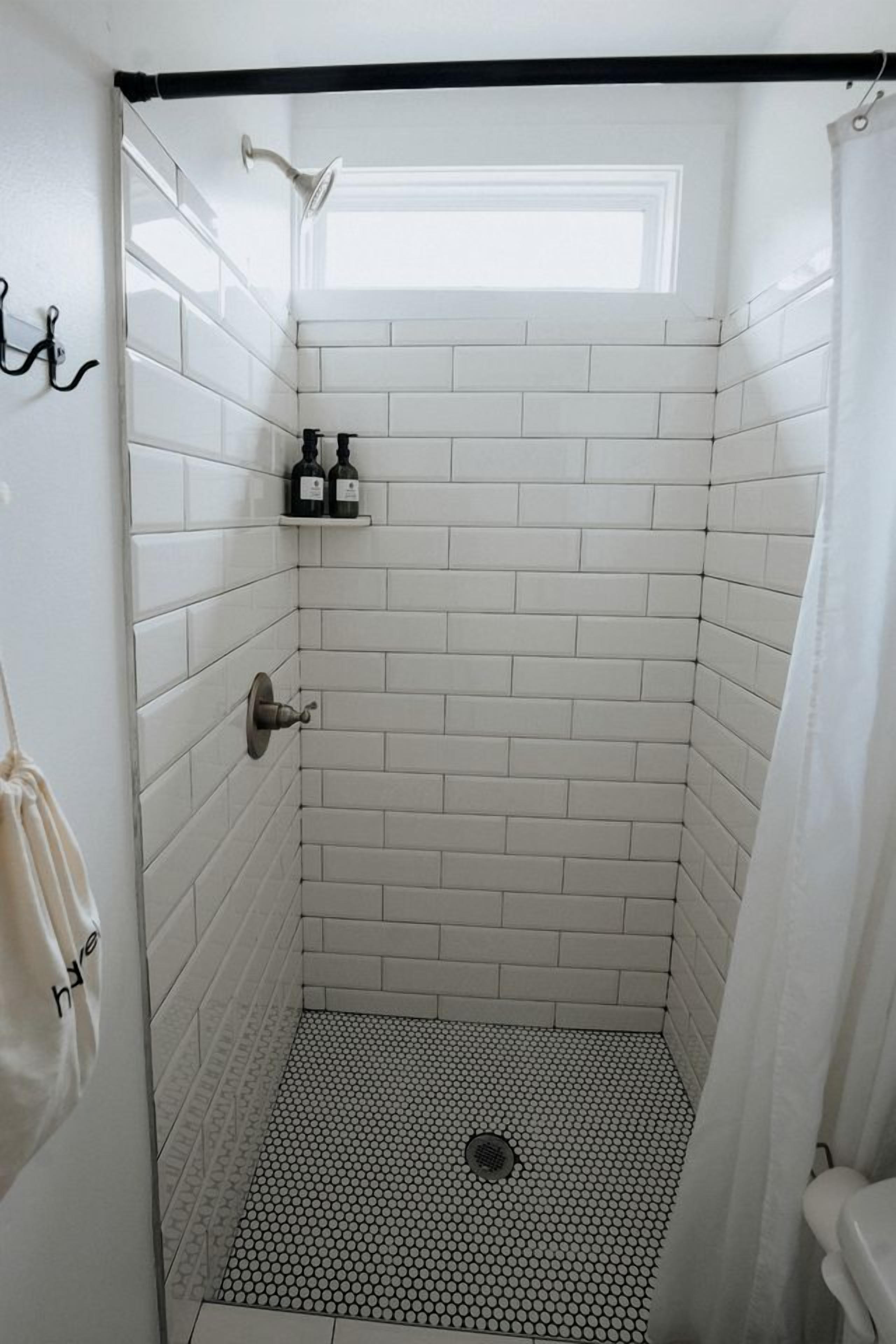 A shower with white subway tiles, a black and white patterned floor, and a small window at the top.