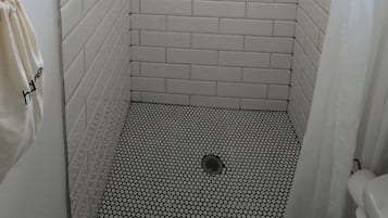 A shower with white subway tiles, a black and white patterned floor, and a small window at the top.