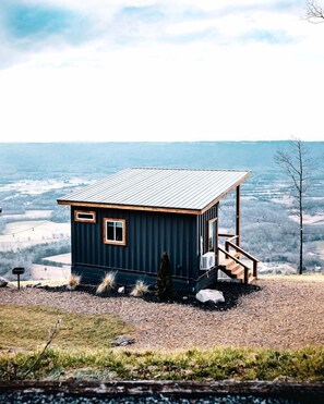 A small cabin with a metal roof, wooden deck, and a single window.