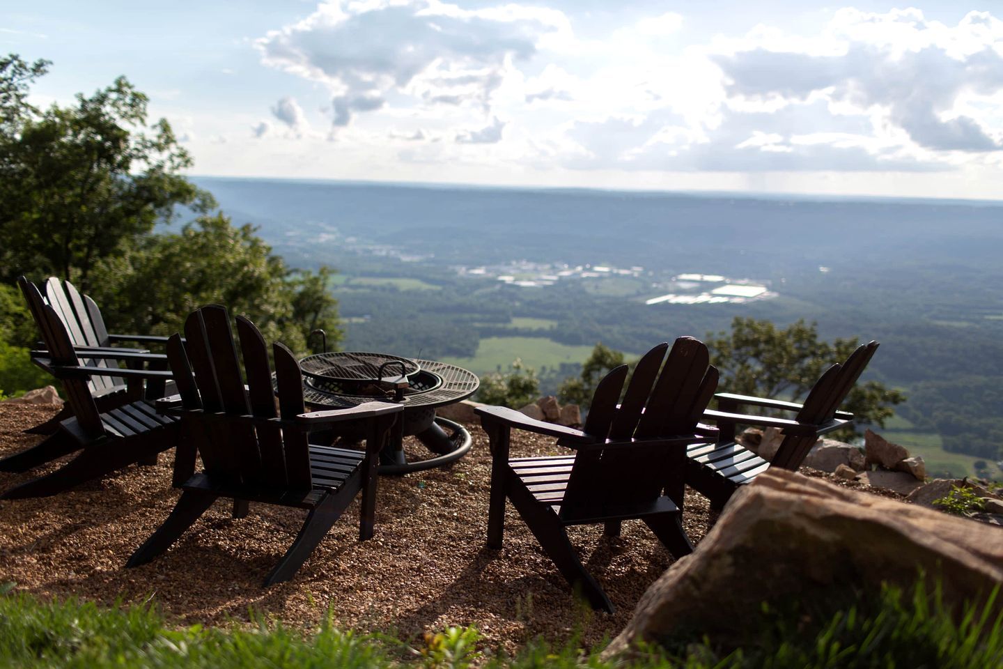 A scenic outdoor seating area with Adirondack chairs and a fire pit overlooking a valley.