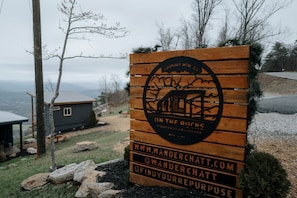 Un letrero de madera con un logotipo y texto para un refugio de montaña, incluyendo una página web y un perfil en redes sociales.