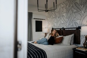 A bedroom with a bed, a headboard, a nightstand, a lamp, and a wall with a leaf pattern. - Unique Container with BBQ Ideal for Couples in Georgia (Rising Fawn)