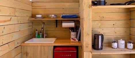 A compact kitchen with wooden walls, a sink, a red refrigerator, and various kitchen utensils and appliances.