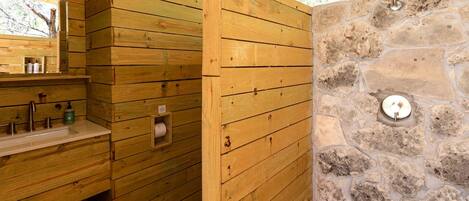 A wooden cabin bathroom with a stone wall, a sink with toiletries, and a mirror.