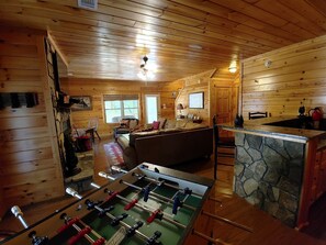 Interior acogedor de una cabaña de madera con mesa de fútbol, barra de piedra y zona de estar confortable.