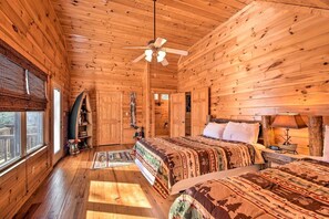 Un dormitorio de cabaña de madera con una cama, un ventilador de techo, una mesita de noche y una ventana.