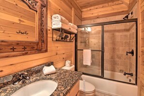A wooden cabin bathroom with a granite countertop sink, a glass-enclosed shower, and a white toilet. - Incredible Cabin with Fireplace and Hot-tub Next to Hiking Trails in Mineral Bluff, Georgia (Mineral Bluff)