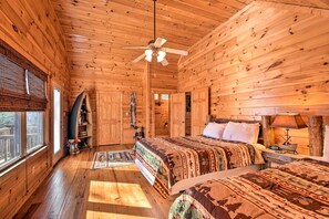 A log cabin bedroom with a bed, a ceiling fan, a nightstand, and a window.