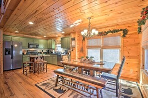 Interior de una cabaña de madera con cocina, comedor y ventanas amplias.