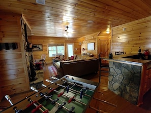 A cozy wooden cabin interior with a foosball table, a stone bar, and a comfortable seating area.