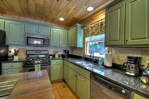 A kitchen with green cabinets, a microwave, stove, sink, and a coffee maker.