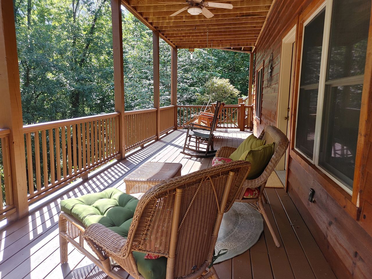 A covered porch with wicker furniture, a ceiling fan, and a view of the surrounding trees.