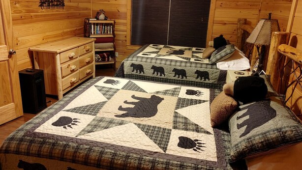 Une chambre de style cabane avec des murs en bois, un lit orné d’un motif matelassé représentant un ours, une commode et une bibliothèque.