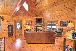 A log cabin interior with a stone fireplace, leather sofa, and a television.