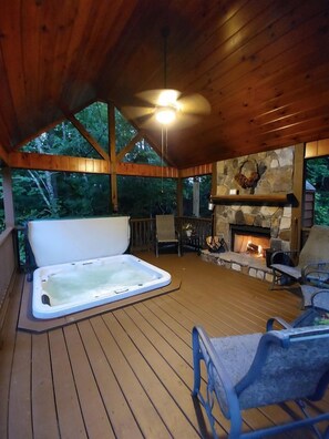 Una terraza de madera con jacuzzi, chimenea de piedra y asientos al aire libre.