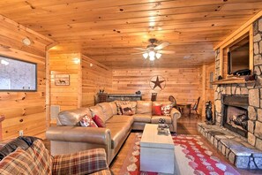 A log cabin interior with a leather sofa, a fireplace, a ceiling fan, and a star decoration on the wall.