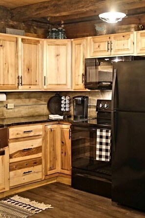 Une cuisine avec des meubles de rangement en bois, un réfrigérateur noir, un four à micro-ondes et une machine à café.