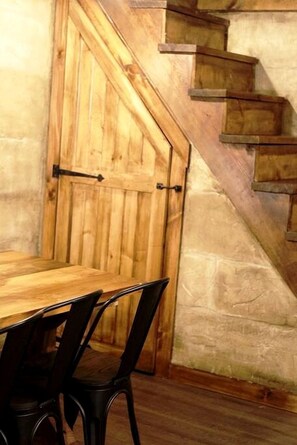 A wooden table with chairs, a wooden door, and a staircase against a stone wall.