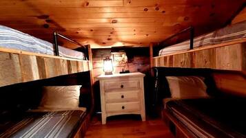 A narrow, wooden-paneled room with bunk beds on either side and a central dresser.
