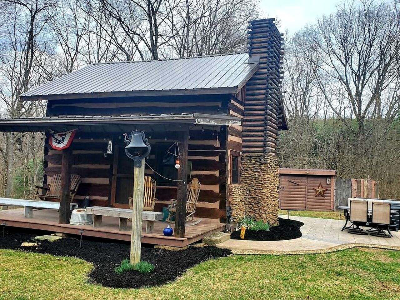 Een vakantiehuis van hout met een metalen dak, een stenen schoorsteen en een terras met tuinmeubilair.