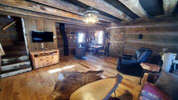 L’intérieur d’un chalet rustique est agrémenté d’un escalier en bois, d’un téléviseur à écran plat, d’un canapé en cuir et d’un coin repas.