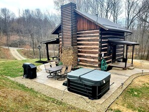A log cabin with a stone chimney, outdoor seating, and a hot tub.