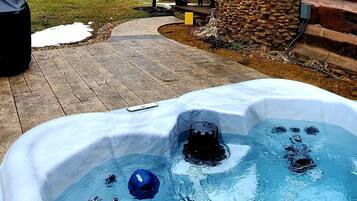 Un bain à remous doté d’une télécommande, entouré d’un mur en pierre et d’une terrasse en bois.