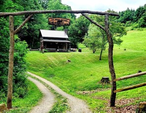 En rustik hytte med skilten 'The Brock Cottage', forbundet med en jordvej, omgivet af frodig vegetation.