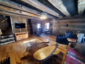Ein rustikales Ferienhäuschen im Inneren mit einer Holztreppe, einem Flachbildfernseher, einem Ledersofa und einem Essbereich.