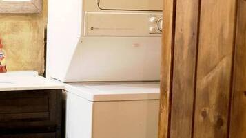 A laundry area with stacked washing machines, a wooden cabinet, and a window with blinds.