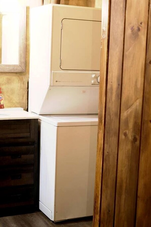 A laundry area with stacked washing machines, a wooden cabinet, and a window with blinds.