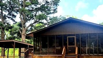 Eine Holzhütte mit Veranda und großen Fenstern, umgeben von Bäumen.
