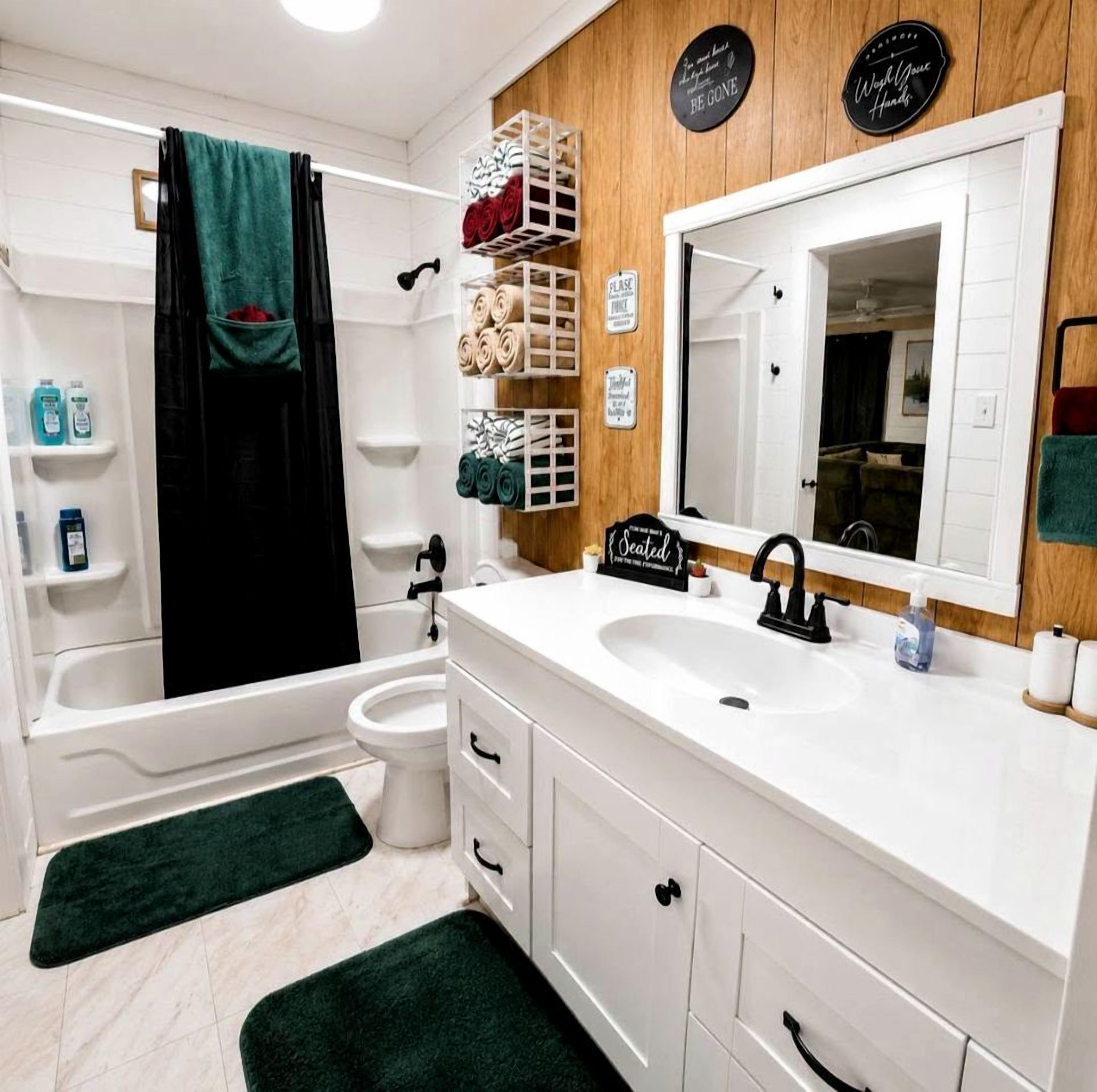 Une salle de bain moderne avec une baignoire, des toilettes et un lavabo. Des serviettes et des articles de toilette sont disposés sur des étagères.