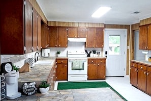 A kitchen with wooden cabinets, a white stove, a coffee maker, and a green rug.