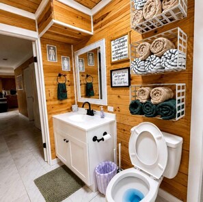 A bathroom with a wooden wall, a white sink, a toilet, and towels on shelves.