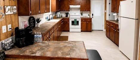 Una cocina con armarios de madera, una isla central, una cafetera y un cubo de basura.