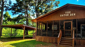 Un bâtiment en bois portant l’inscription « The Gator Den », doté d’un espace extérieur couvert avec des sièges et d’un escalier menant à l’entrée.