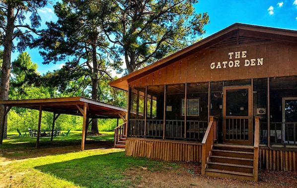 Een houten gebouw met de naam 'The Gator Den', voorzien van een overdekte buitenzitplaats en een trap naar de ingang.