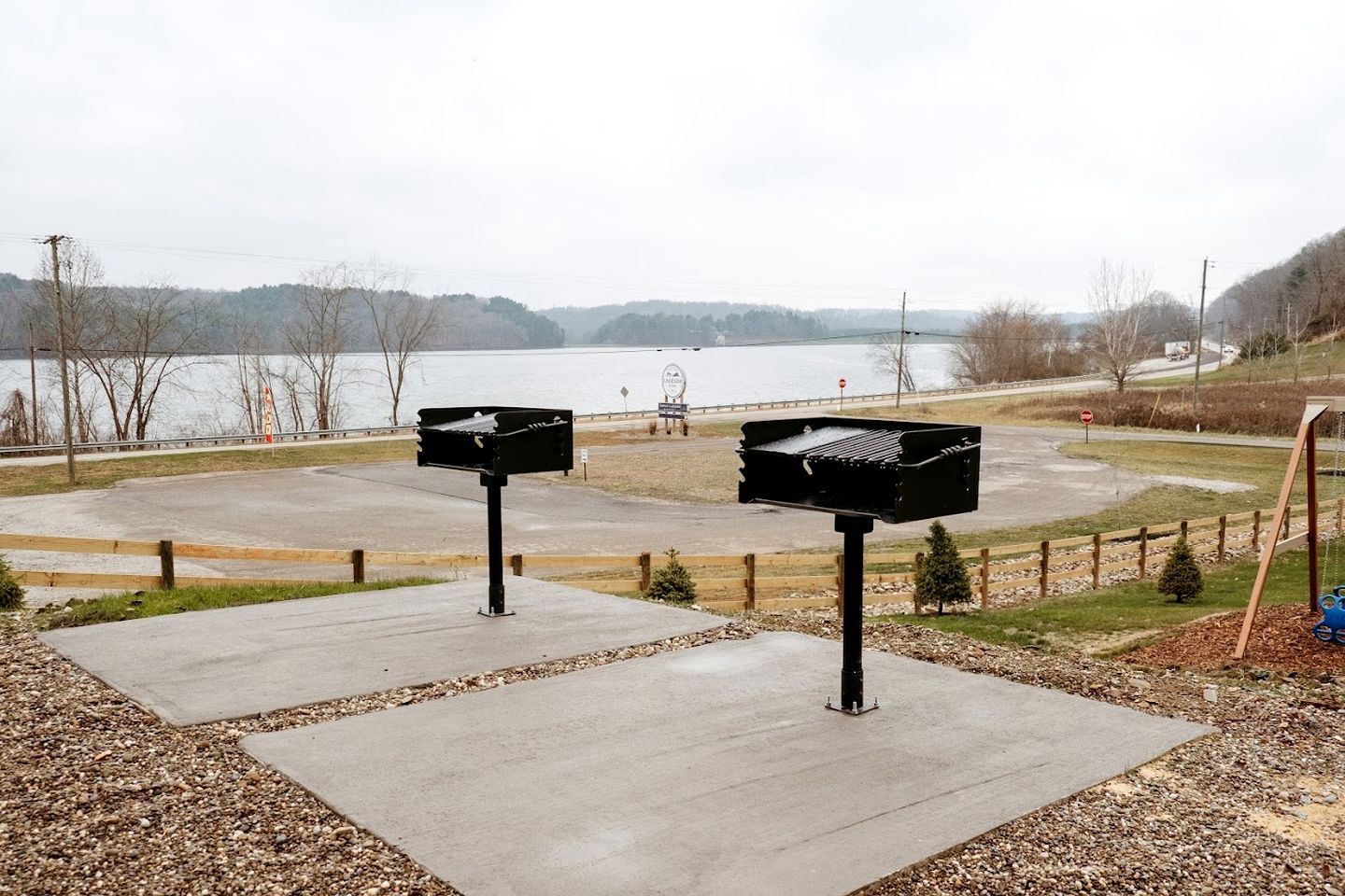 A parking area with two black mailboxes, a swing set, and a view of a lake.
