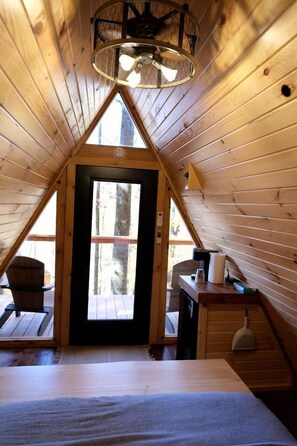 Un intérieur en bois avec un plafond en pente, un lit, un bureau et une porte donnant sur l’extérieur.