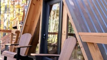 A wooden A-frame cabin with a glass door, two wooden chairs, and a deck.