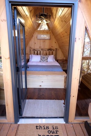 A wooden cabin with a loft bed, a small bedside table, and a hanging light fixture.
