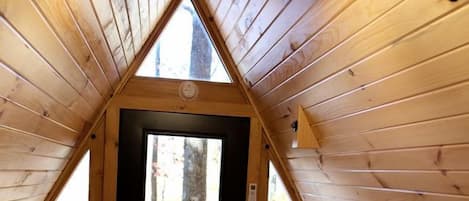 Ein Holzinnenraum mit schrägem Dach, einem Bett, einem Schreibtisch und einer zur Außenwelt führenden Tür.
