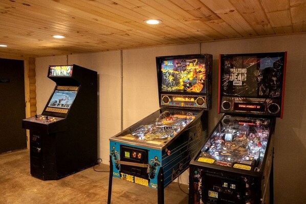 Una habitación con tres máquinas de pinball, techo de madera y paredes blancas.