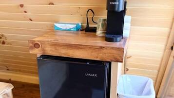Ett litet, praktiskt kök med ett svart kylskåp, en kaffebryggare och en papperskorg.