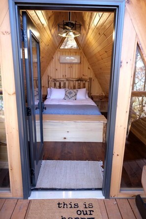 Une cabane en bois avec un lit en mezzanine, une petite table de chevet et un luminaire suspendu.