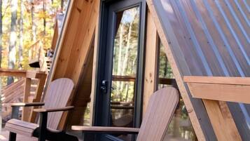Uma cabana em A de madeira com porta de vidro, duas cadeiras de madeira e um deck.